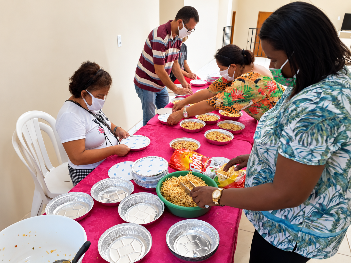 Voluntários preparando e embalando refeições comunitárias em uma mesa longa